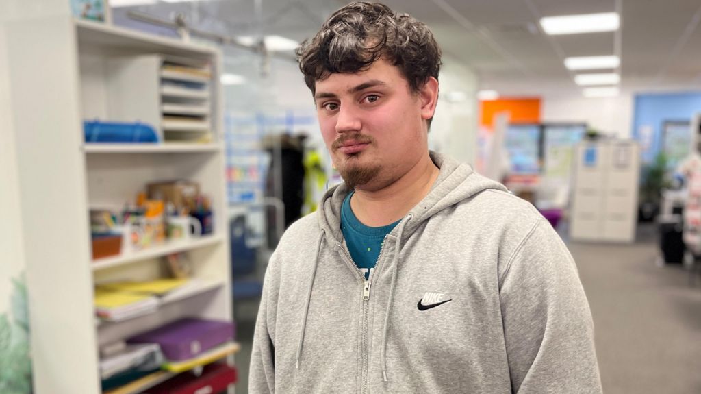 Terry, aged 22, has dark hair and a goatee. He is wearing a grey zip hoodie over a teal t-shirt