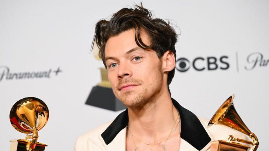 Harry Styles looks at the camera whilst holding two GRAMMY award trophies.