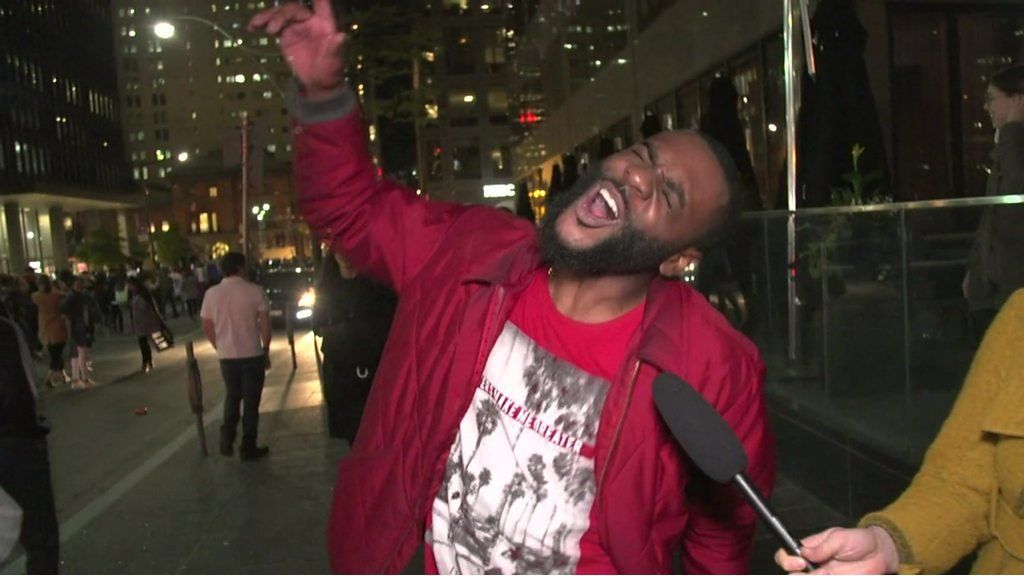 A fan exclaims to the sky with his eyes closed and right hand raised while being interviewed on Toronto's streets
