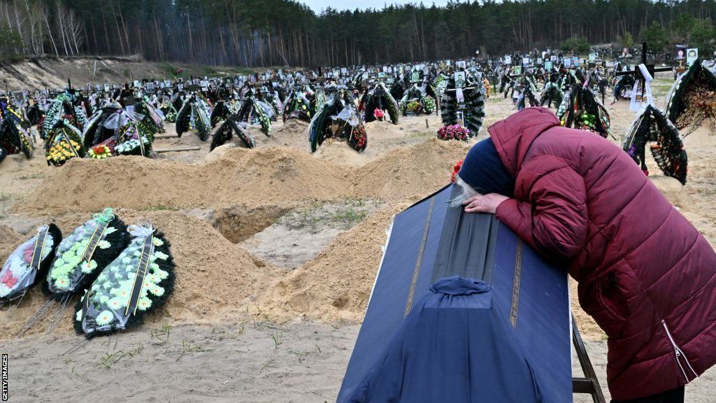 A woman cries on a coffin in a cemetery in Irpin