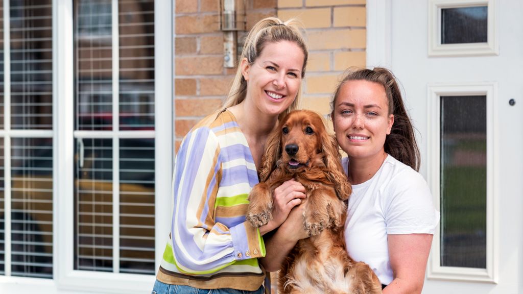 Two women and a dog outside a house