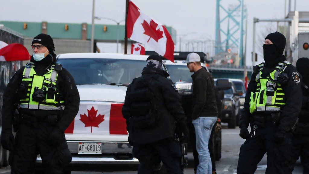 Police officers stand guard on a street as truckers and supporters continue blocking access to the Ambassador Bridge