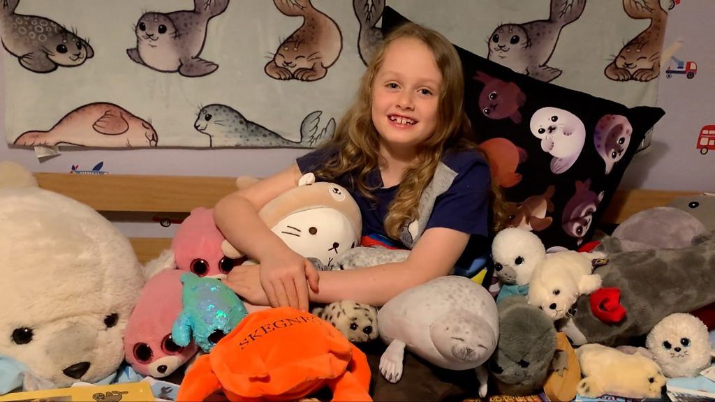 Child sitting on bed surrounded by soft toys