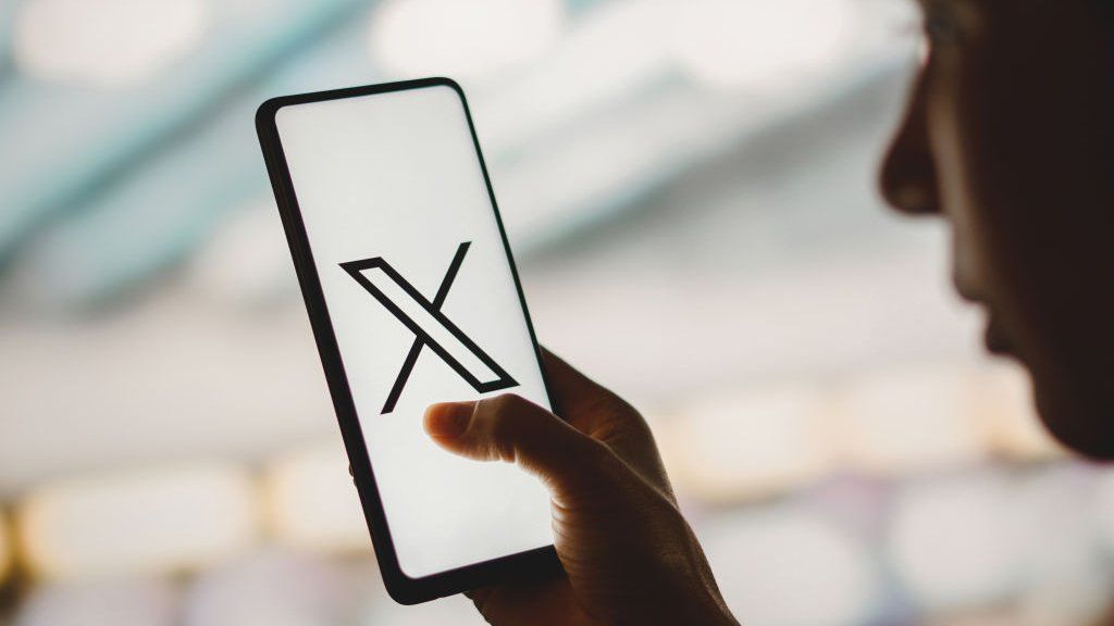 A photo illustration of someone looking at the X app on a phone