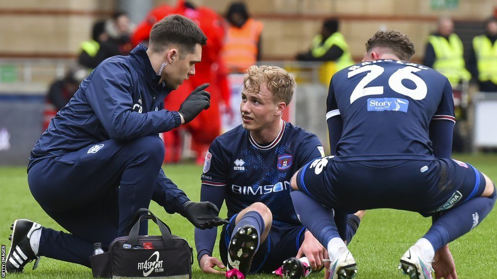 Fin Back (centre) getting treatment from a physio while playing for Carlisle