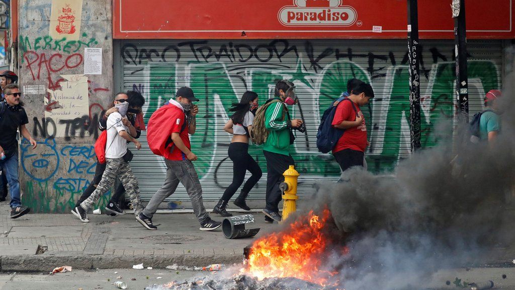 Protesters walk quickly past burning debris on the streets of Santiago