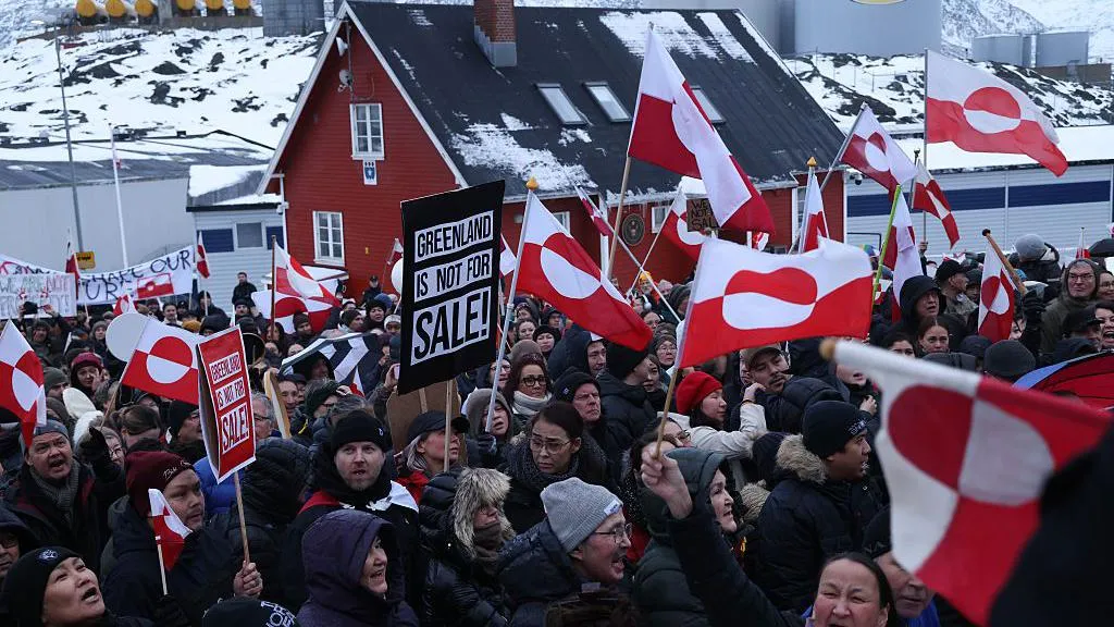 Greenlanders protesting in front of the US Consulate in Greenland. There are dozens pictured, holding up Greenland flags and signs that say 