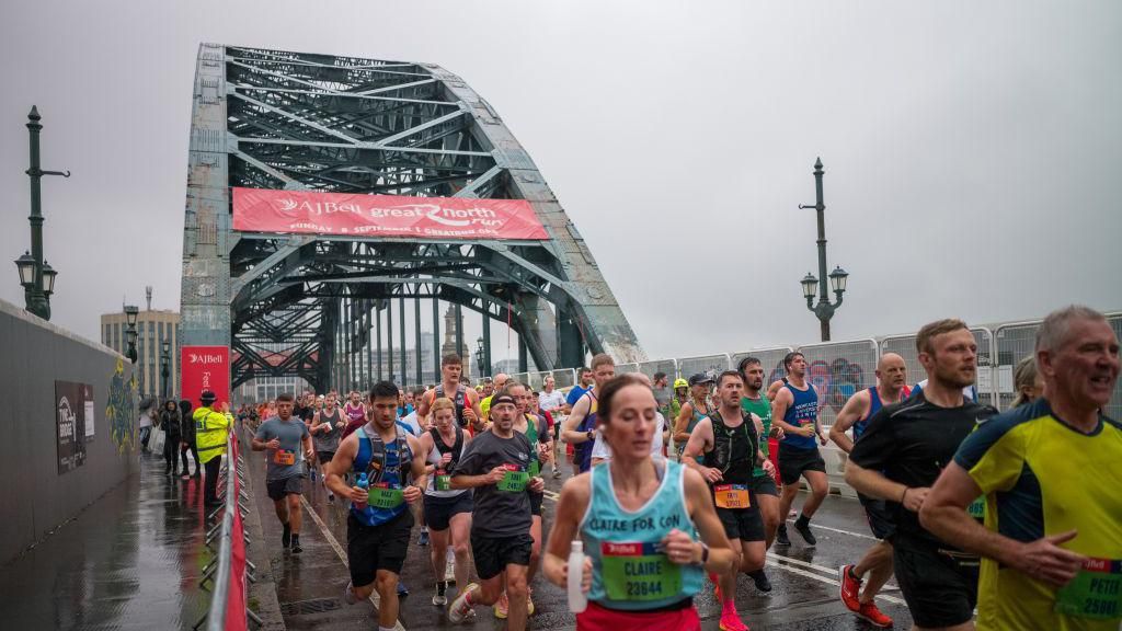 Hundreds of runners, wearing different coloured vests, cross the Tyne Bridge in the rain during the 2024 Great North Run.