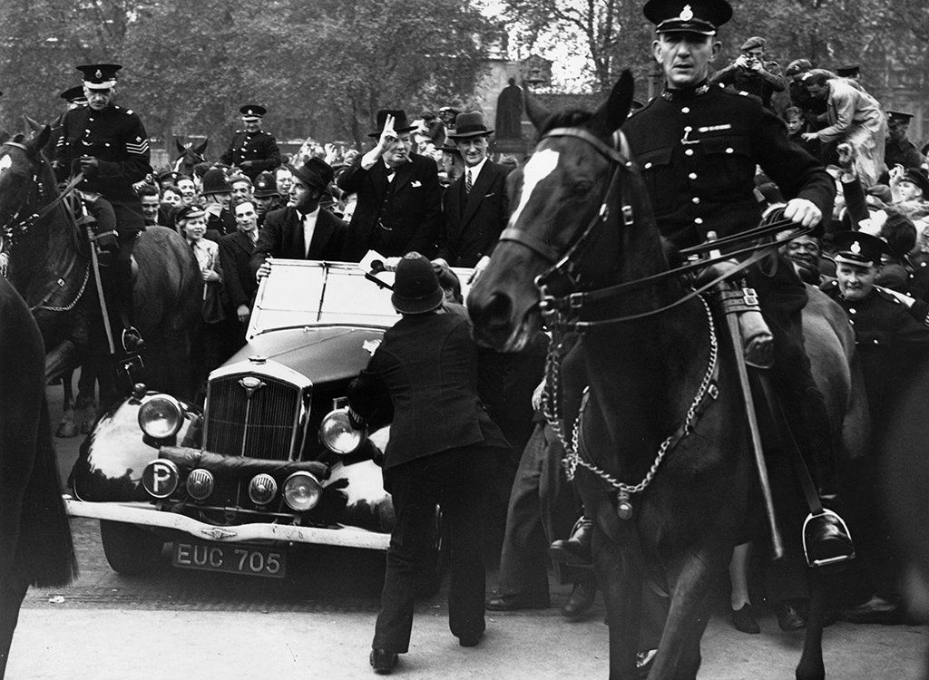 Prime Minister Winston Churchill rides in an open car to the House of Commons, surrounded by celebrating crowds on VE Day, 1945