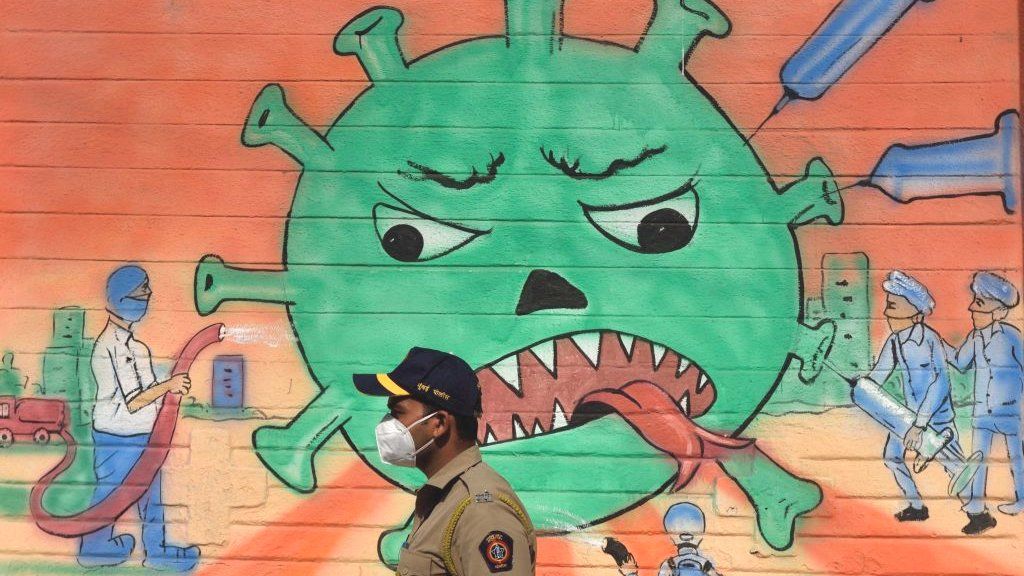 A policeman walks past a mural of frontline warriors attacking the gigantic coronavirus,
