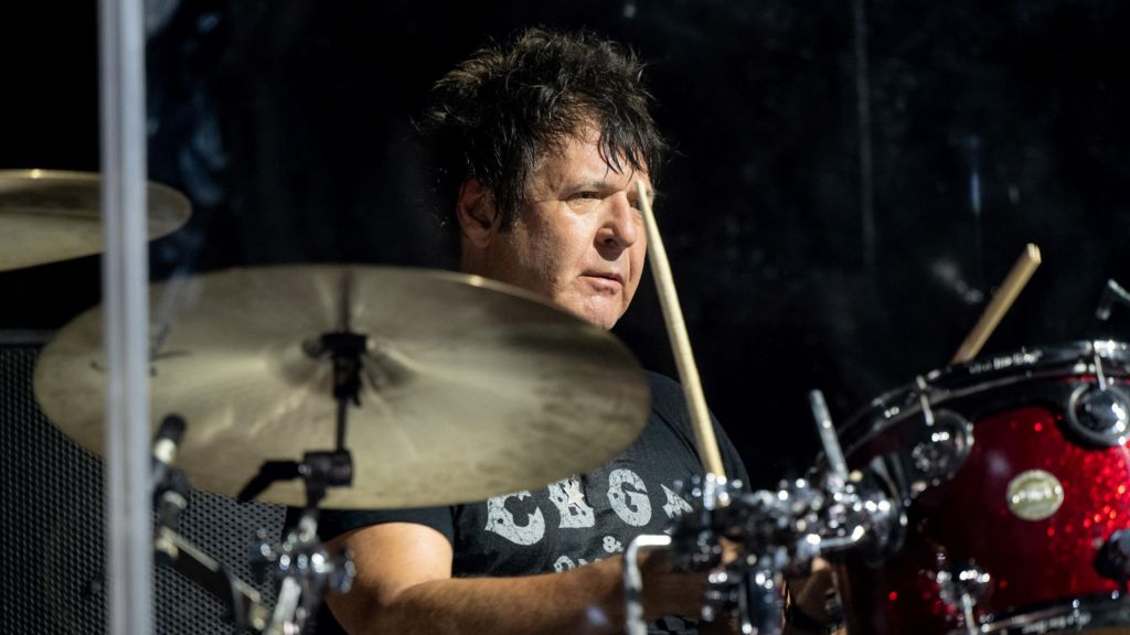 Clem Burke playing the drums at Coachella in 2023. He is wearing a black CBGB club T-shirt and has short black hair.