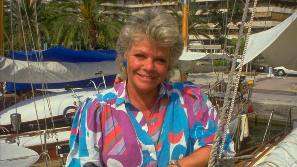Judith Chalmers in a bright multi-coloured blouse in front of a Mediterranean harbour on Wish You Were Here?