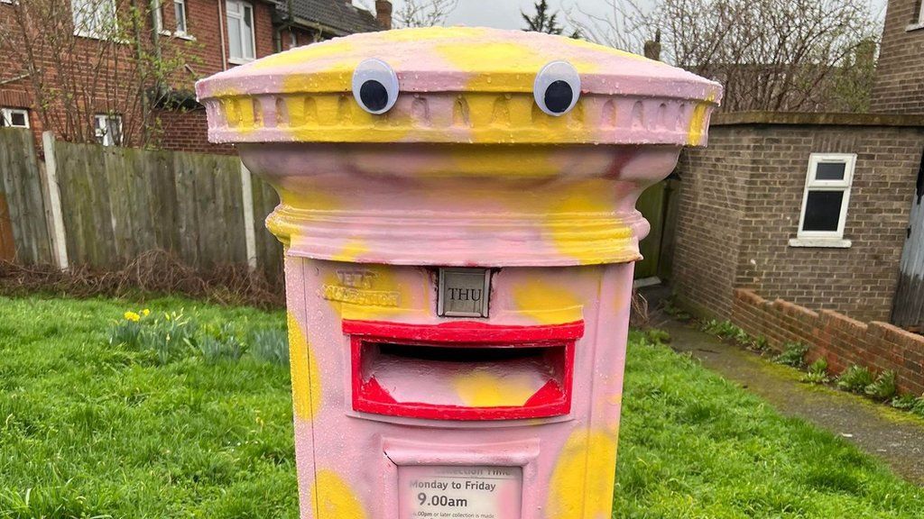 A postbox that has been painted pink with yellow spots, and had googly eyes and red lips added to look like Mr Blobby