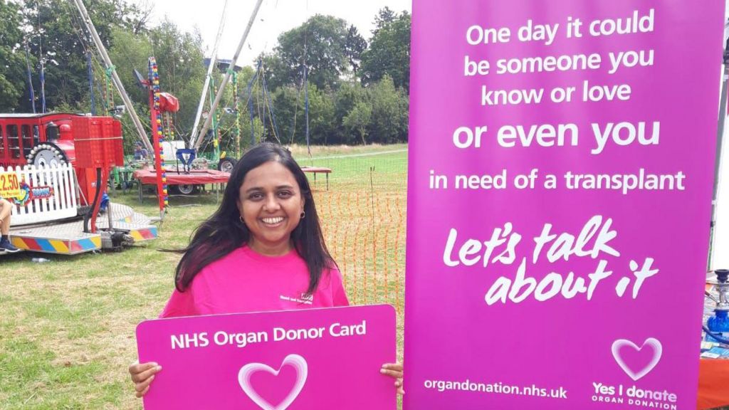 Dishna Hirani holding a giant NHS Donor Card and standing in front of a banner for NHS organ donation at an outreach event