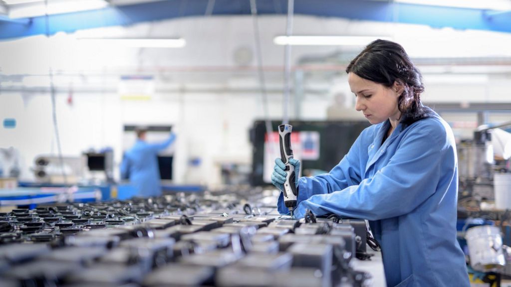 Female worker in blue overalls assembling components in circuit board assembly factory