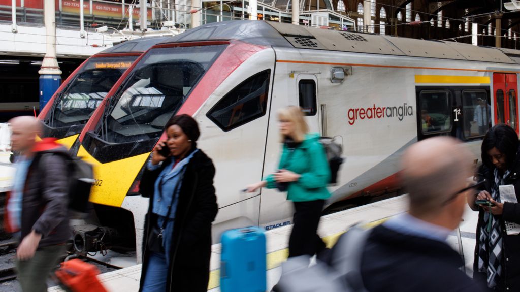 A Greater Anglia train at London Liverpool Street, passed by passengers on the platform
