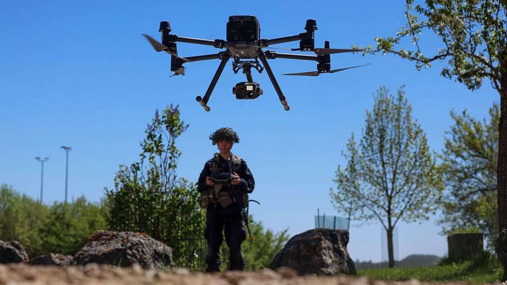 A soldier from the US Army in full combat gear stands in the background piloting a drone in a simulated village during the Combined Resolve "Greywolves" exercise at the US military Hohenfels Training Area in Hohenfels, Germany, on Thursday, April 30, 2026.