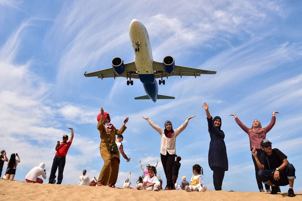 Tourists pose for a picture on Mai Khao Beach, Thailand as a plane lands at Phuket International Airport.