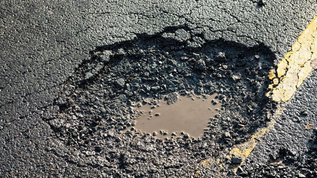 A close up of a pothole on a double yellow lined road with muddy water in the bottom