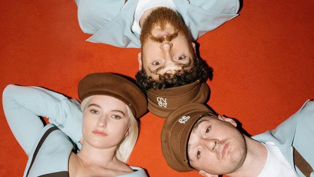 Promotional photo for Clean Bandit, showing the band lying on a red carpet in a clockwise arrangement