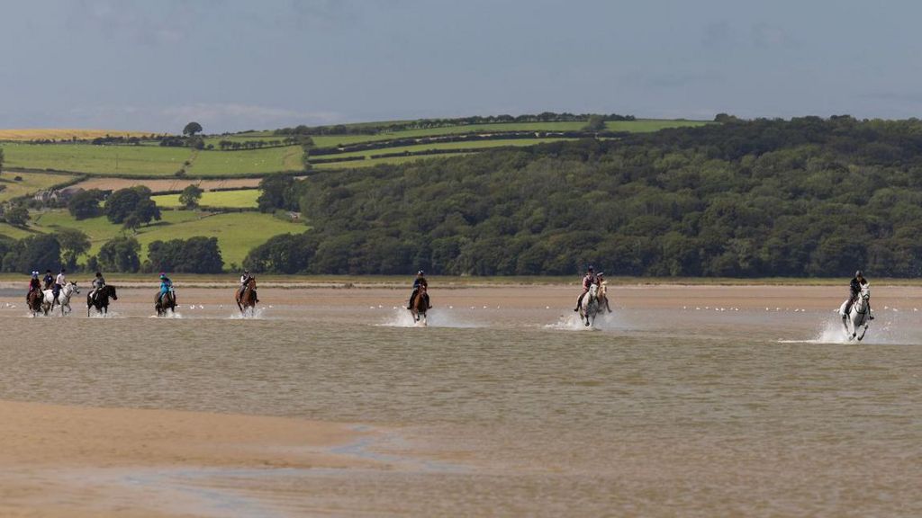 riders gallop across the bay with fells in the background