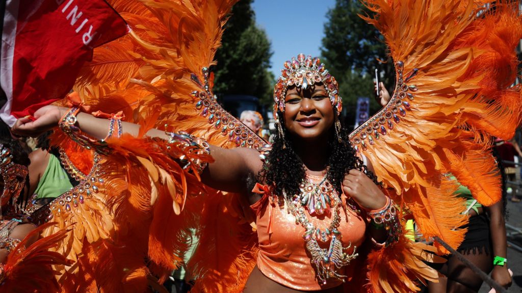 A woman in an orange costume with beads and feathers.