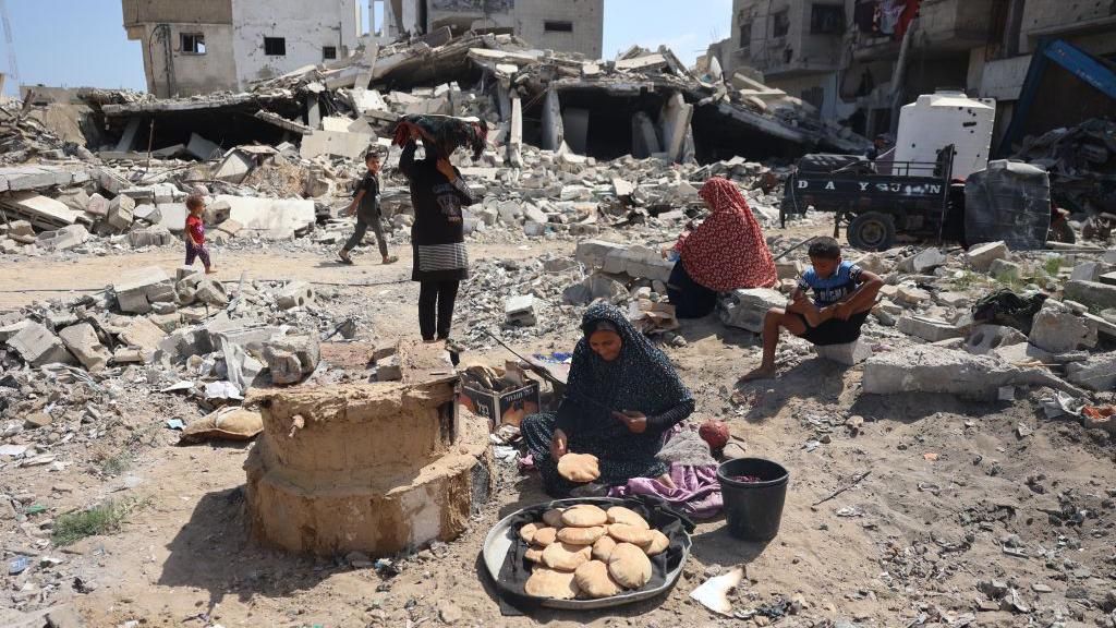 A Palestinian woman bakes bread amid the rubble of destroyed buildings in the southern Gaza city of Khan Younis (30 June 2024)