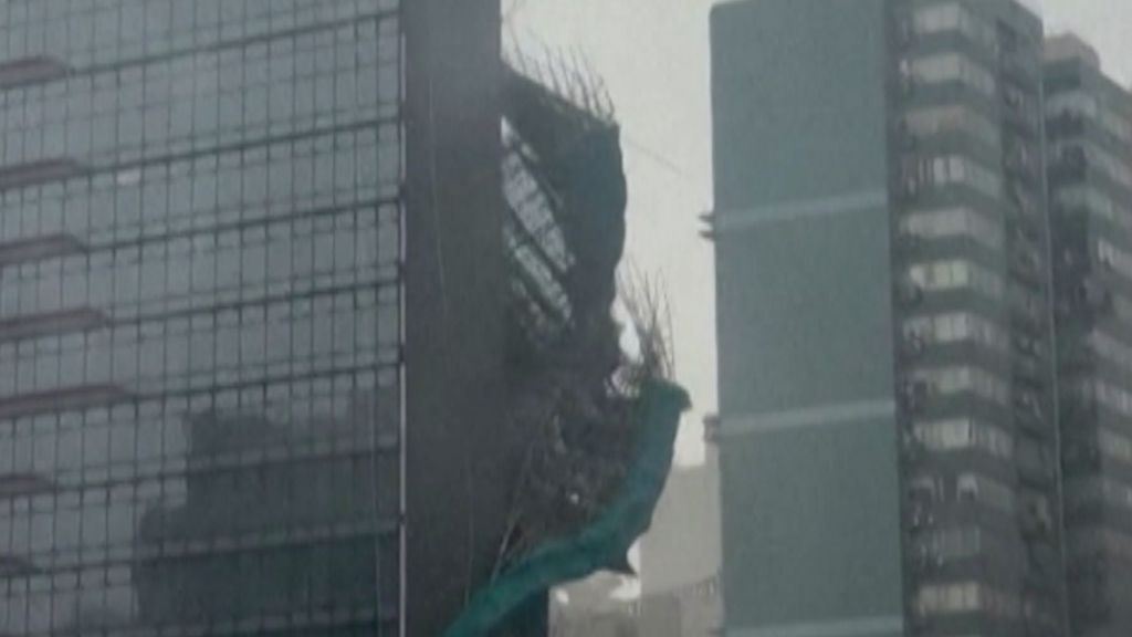 Bamboo and green plastic sheeting are seen falling down the side of a glass skyscraper.