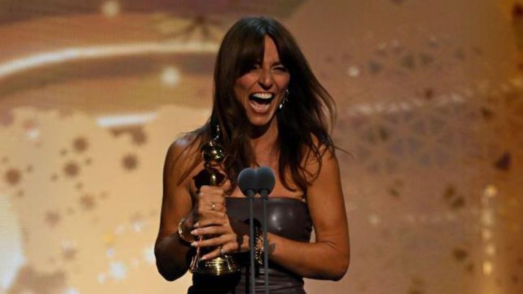 Davina McCall in a long evening dress, smiling and holding her award on stage