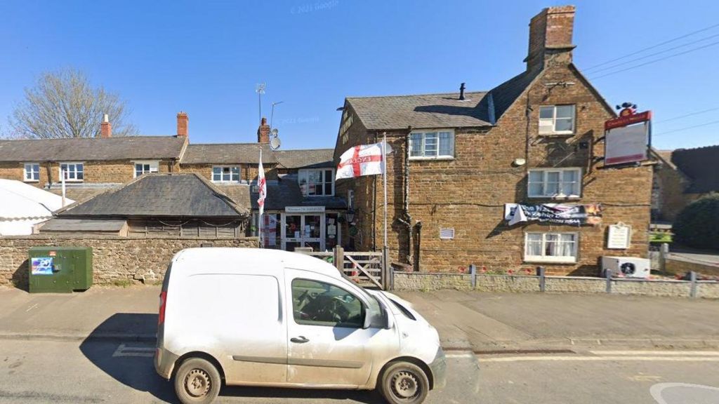 Village street showing green equipment cabin, pub and white van