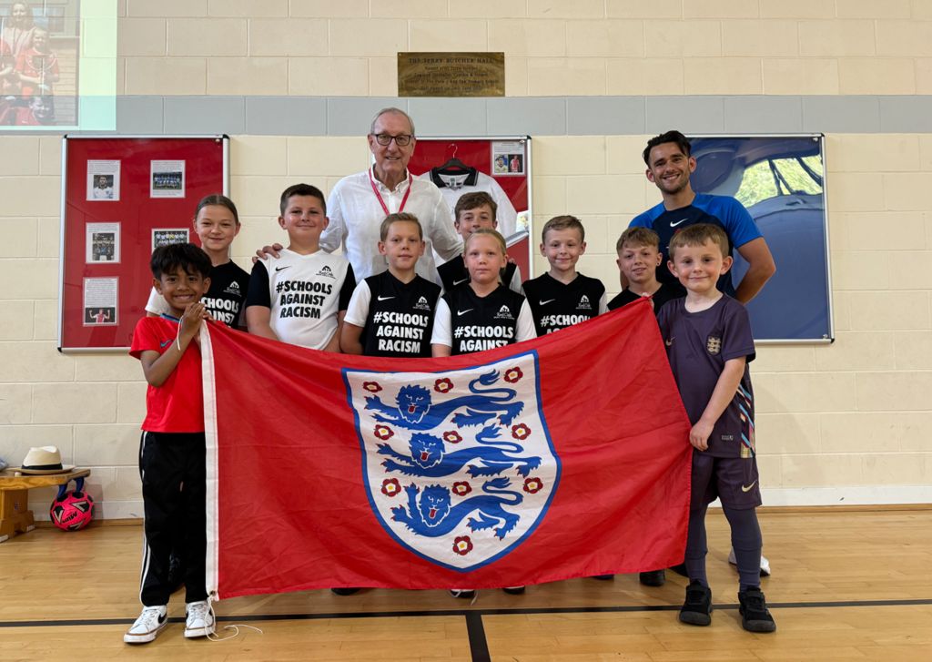 Terry Butcher with young students and a large red England flag with the Three Lions badge on 