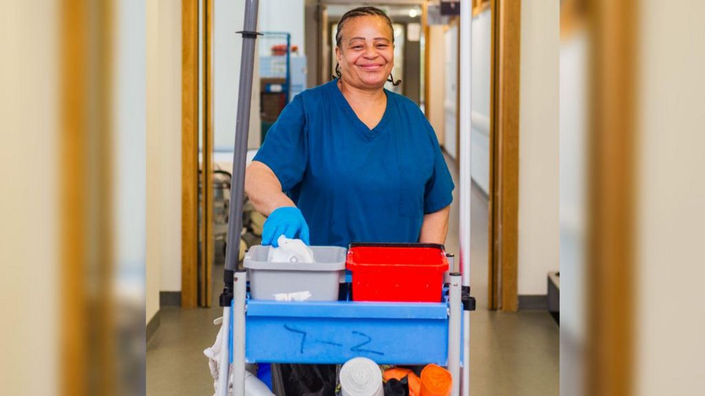 A cleaner standing in the hospital hallway leaning on a cart with cleaning supplies