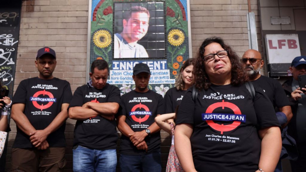 Family members of Jean Charles de Menezes stand in front of a memorial to him. Patricia Armani da Silva stands at the front. 