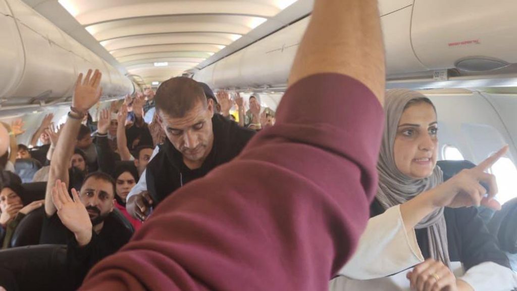 Passengers, including men and women,  raise their hands in a plane 