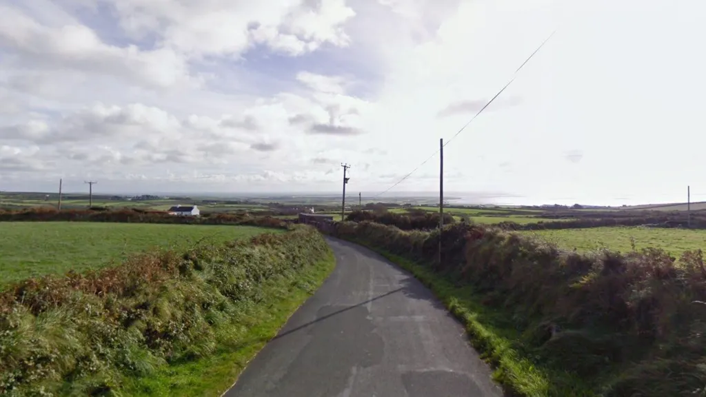 The road, it is a country lane, there are fields around and houses dotted across the landscape.