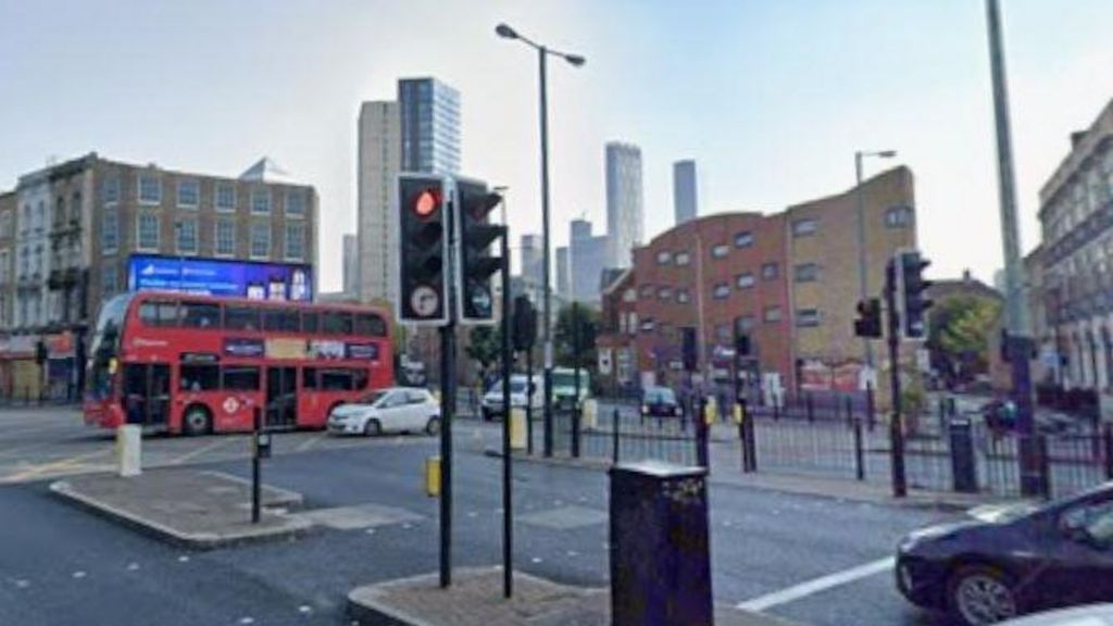 A busy road junction in east London, there are cars and red buses on the roads and high-rise commercial and residential buildings in the background.