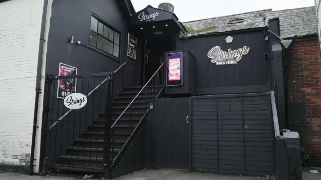 The exterior of Strings, which is painted black, with stairs leading up to the entrance.