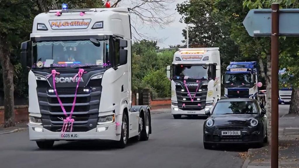 Truck cabs with pink ribbons on their front driven down road