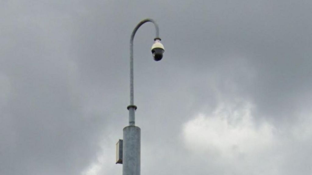 Close up of a black domed camera hanging from a hooked grey lamppost
