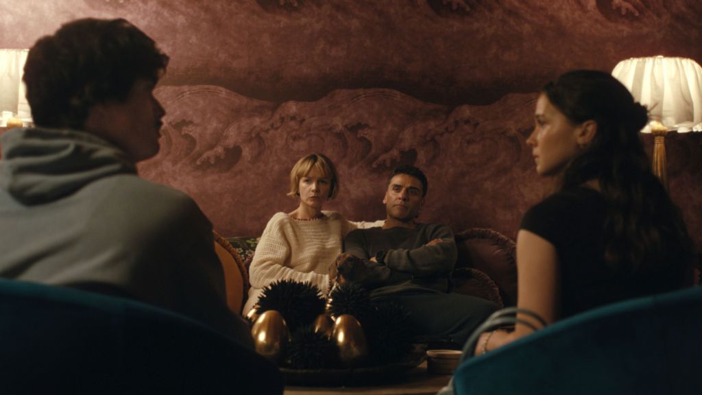 Carey Mulligan and Oscar Isaac sit together on a sofa, looking at a younger couple, played by Charles Melton and Cailee Spaeny ,who are looking at each other 