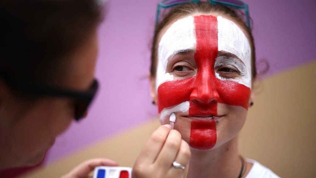 A woman having her face painted with the England flag