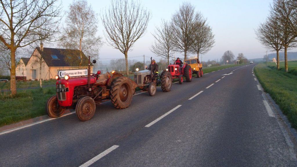 A convoy of vintage tractors on a country road in Normandy, France