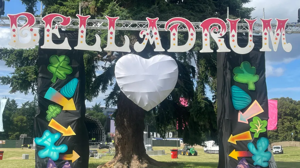 A large free-standing sign advertising Belladrum festival. There's a stage on a field in the background. 