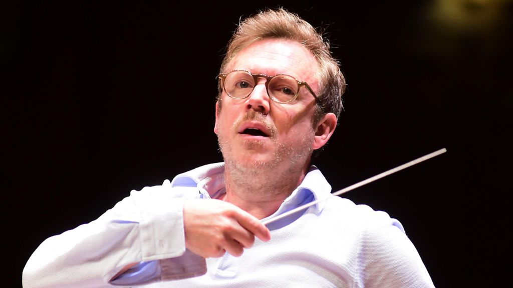Daniel Harding in an open-necked white shirt with an arm raised holding a conductor's baton conducting the Orchestra Santa Cecilia of Roma in Bologna on 8 May 2026