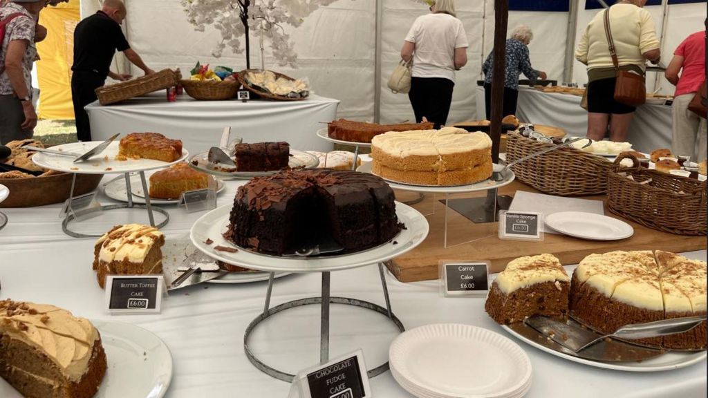 A large white table with different varieties of cake on plates and cake stands inside a marquee