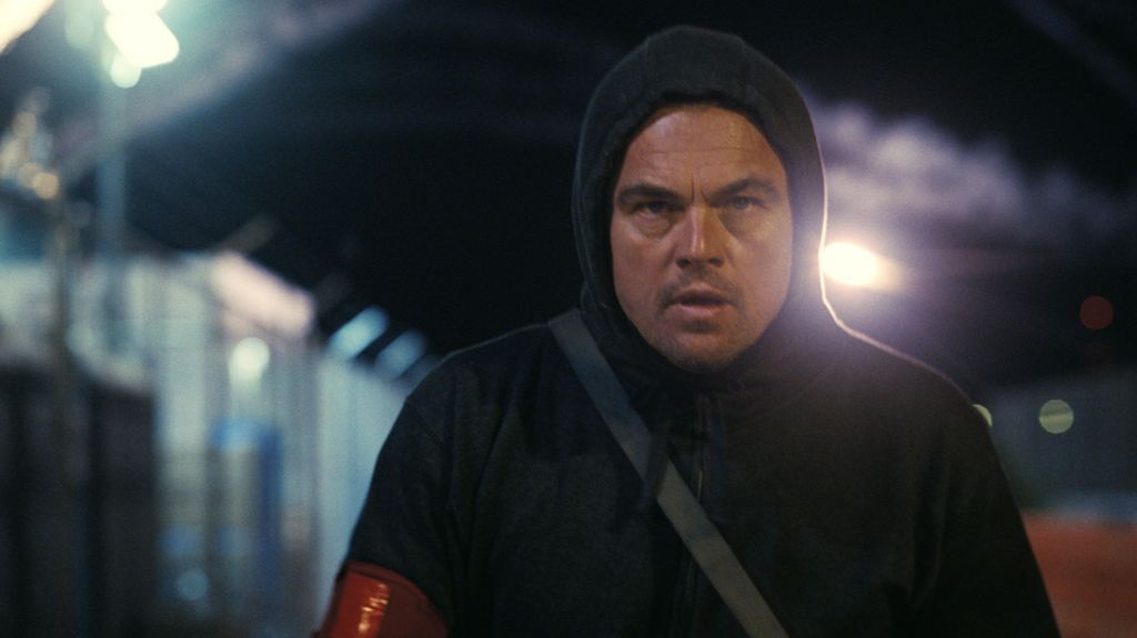 A still from One Battle After Another showing Leonardo DiCaprio's character wearing a black hoodie and walking intently at night