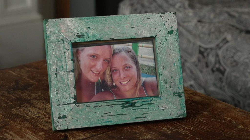A photograph of Catherine and Annabel from when they were younger, inside a green wooden frame, sits on top of a coffee table. They both have blonde hair, are wearing summer clothes and are smiling.