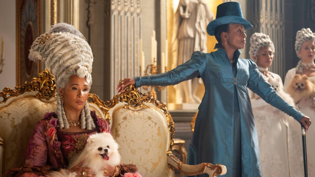 Queen Charlotte (Golda Rosheuvel), wearing a grey wig with a dog on her lap, and Lady Danbury (Adjoa Andoh) in a blue frock coat and hat.
