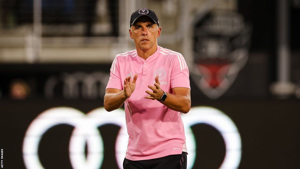 Phil Neville wearing a baseball cap and a pink T-shirt claps his hands