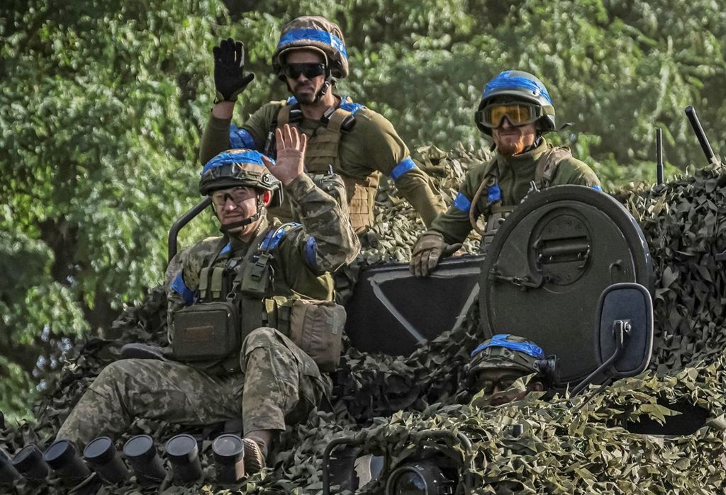 Three Ukrainian soldiers sit on top of tank in Sumy region wearing helmets and military gear with blue stripes, on 11 August